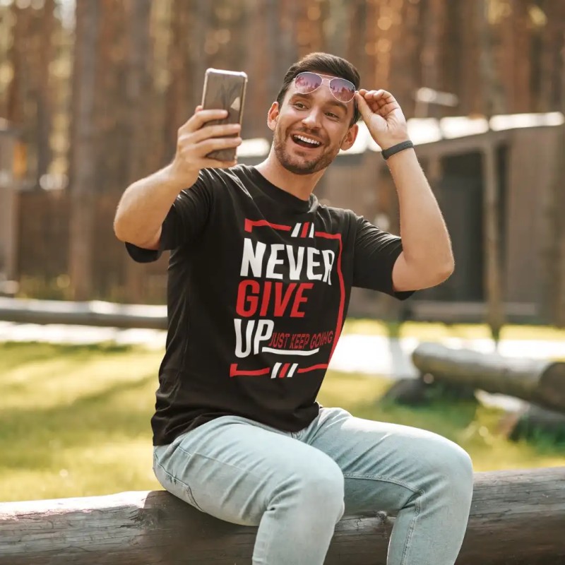 ragazzo che fa selfie su un muretto con addosso la maglietta di ispirazione massima "never give up just keep going" in nero